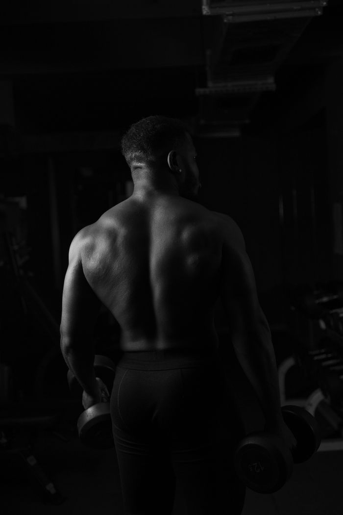 Monochrome image of a muscular man holding dumbbells in a gym, showcasing strength and fitness.